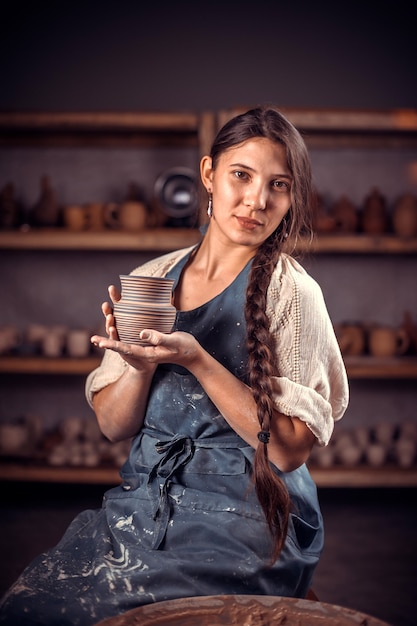 Charmingfemale master siting on bench with pottery wheel and making clay pot