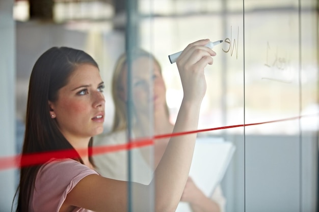 Charting the expected results A young businesswoman writing down plans on a glass pane