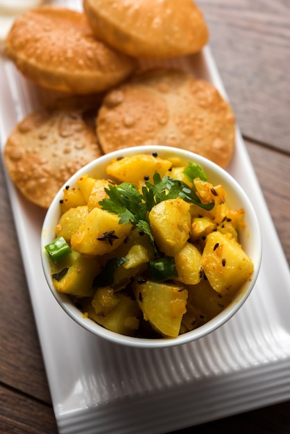 Chatpate Masala Aloo Sabzi fry OR Bombay potatoes served with fried puri or Indian bread made up of wheat in a plate, selective focus