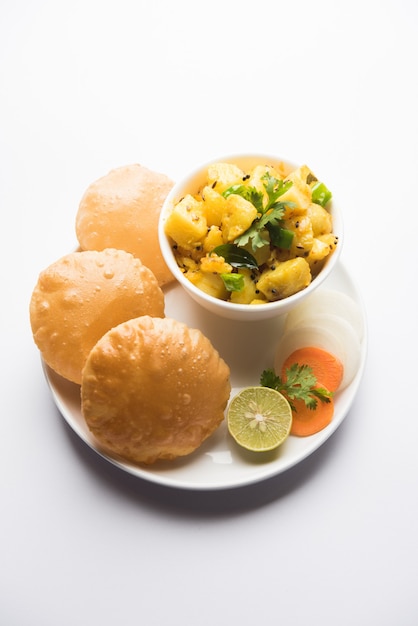 Chatpate Masala Aloo Sabzi fry OR Bombay potatoes served with fried puri or Indian bread made up of wheat in a plate, selective focus