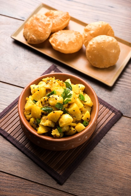 Chatpate Masala Aloo Sabzi 프라이 또는 봄베이 감자는 튀긴 푸리 또는 밀로 만든 인도 빵을 접시에 담고 선별적인 초점을 맞춥니다.