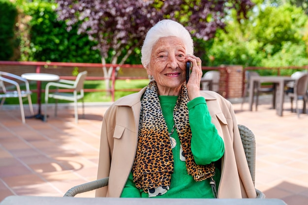 庭に囲まれた老人ホームで家族とモバイルで会話する楽しそうな高齢の祖母