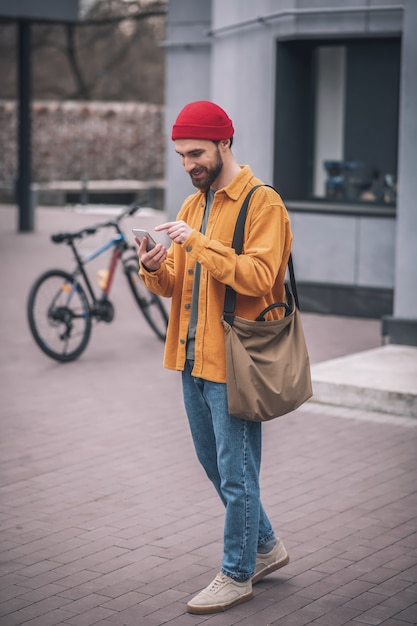 Chatten. Man in een rode hoed en oranje jasje met zijn smartphone in handen