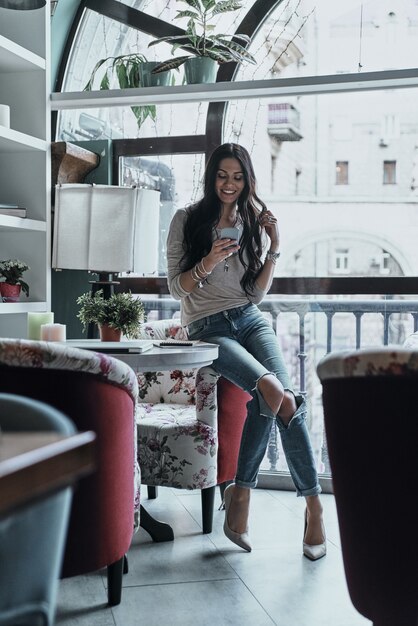 Chatten met vrienden. Volledige lengte van mooie jonge glimlachende vrouw die haar slimme telefoon gebruikt