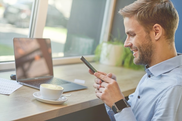 Chatting with friends side view of a freelancer or businessman using his smartphone and smiling