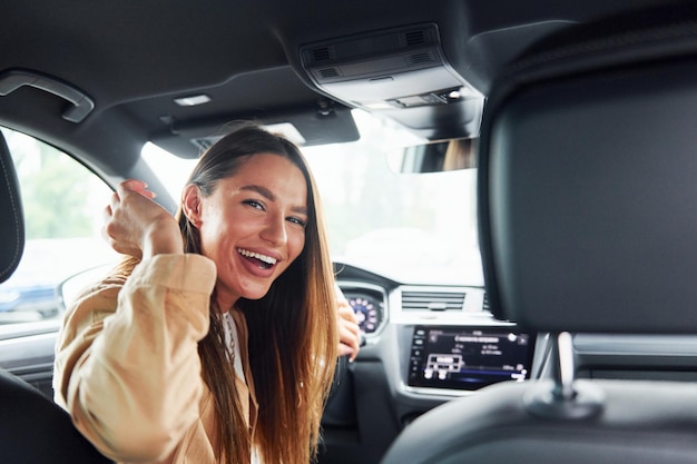 Chauffeur kijkt achterom en glimlacht Modieuze mooie jonge vrouw en haar moderne auto