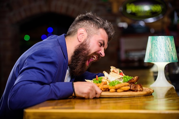Cheat meal concept Hipster hungry eat pub fried food Manager formal suit sit at bar counter Delicious meal Man received meal with fried potato fish sticks meat High calorie snack Enjoy meal