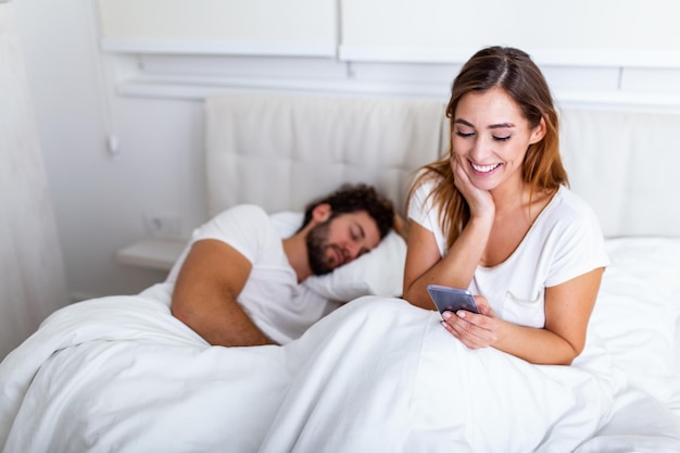 Cheating wife. Beautiful woman chatting privately on cellphone, hiding from her sleeping husband, empty space. Cheating Girlfriend Chatting On Phone While Boyfriend Sleeping In Bedroom At Night.