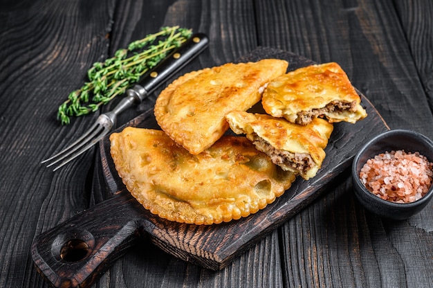 Cheburek meat pastry pie with herbs. Black wooden background. Top view.