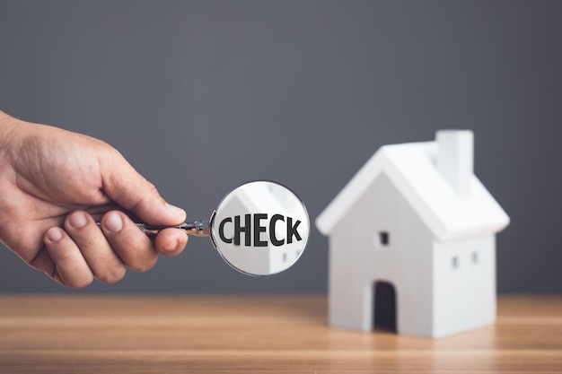 Photo check before home delivery hand holding a magnifying glass and inspecting the house model on wooden desk the concept of finding home problems before signing a contract