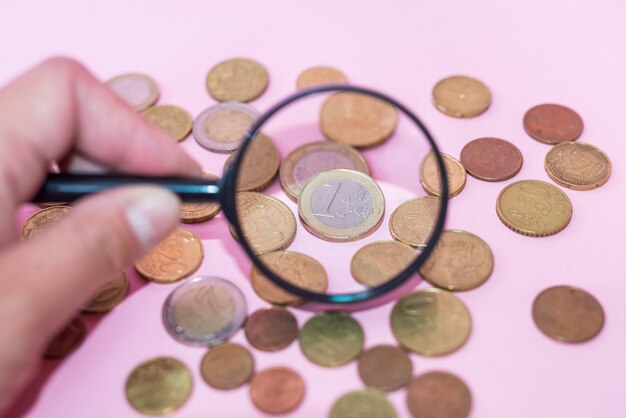 Check coins with a magnifier on a pink background. Euro coins through a magnifying glass.