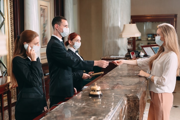 Photo check in hotel. receptionist at counter in hotel wearing medical masks as precaution against virus. young woman on a business trip doing check-in at the hotel