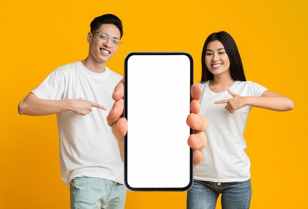 Check This Smiling Asian Man And Woman Pointing At Big Blank Smartphone