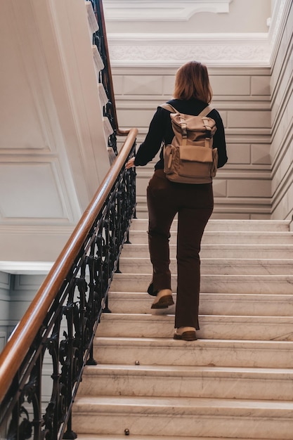 Checkin at the hotel of a traveler with a backpack the woman climbs the stairs a woman with a green backpack climbs a spiral staircase