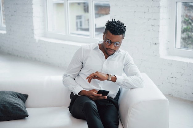 Checking how much time left until the end of the break. Stylish afro american guy in classic wear and glasses