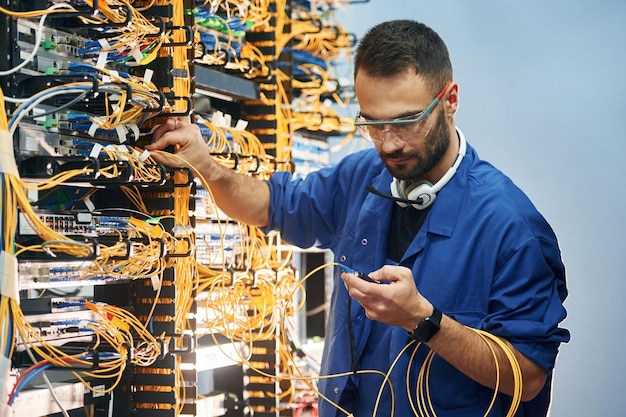 Checking signal by device Young man is working with internet equipment and wires in server room