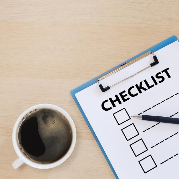 Checklist box on clipboard with pen and coffee cup on wooden\
table. check choice answer test. checklist information\
writing.