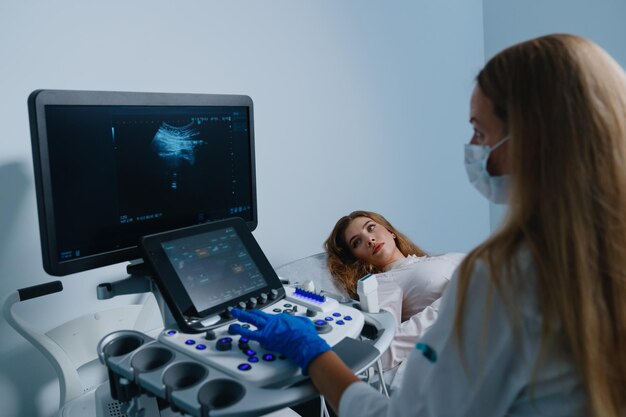 사진 병원에서 건강 검진 의사는 현대 초음파 기계를 사용하여 젊은 여성 환자를 검사합니다