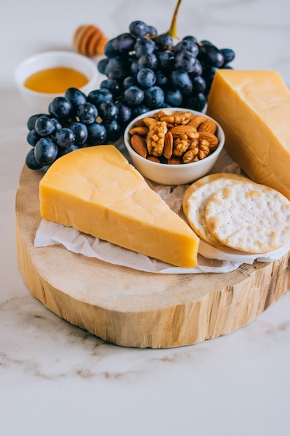 Formaggio cheddar, uva, noci, miele e cracker in tavola di legno su marmo