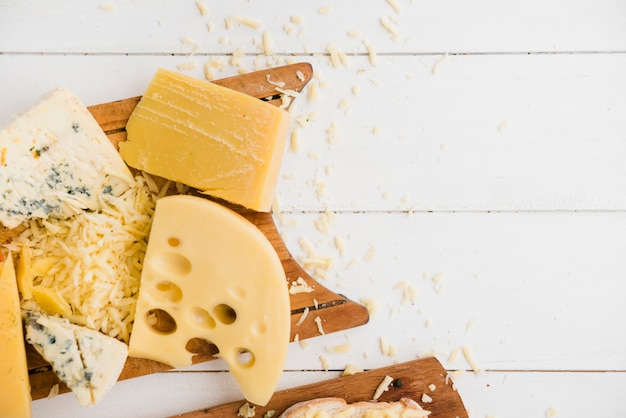 Cheddar; maasdam and blue cheese on chopping board over the table