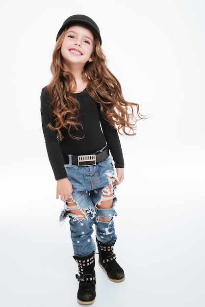 Cheeful curly little girl in hat and torn jeans