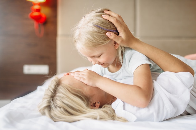 陽気な母と子が自宅のベッドに横たわってかくれんぼをします。親の気持ち、一体感、母性