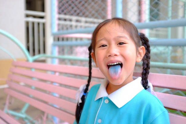 Cheeky funny face little Asian child girl smile and poking out blue colored tongue.