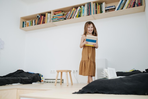 Cheeky little girl walking on an elevated wooden floor with a book in her hands