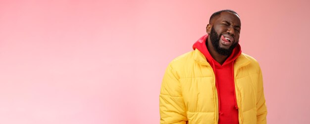 Photo cheeky stylish funny african bearded man in yellow trendy jacket red hoodie show tongue sassy flirty