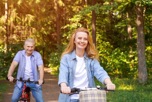 Cheerful active senior couple with bicycle walking through park together