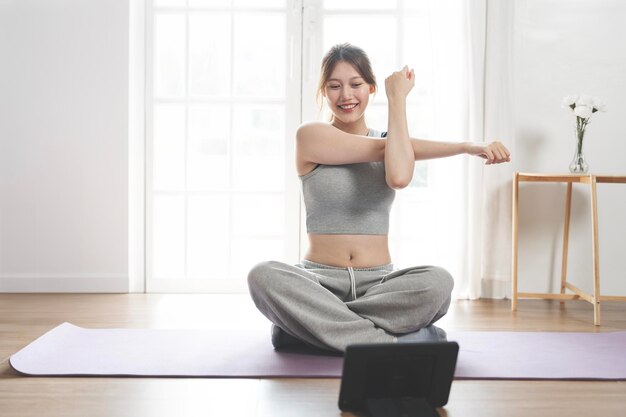 家でフィットネスをしている陽気で活発な女性が床に座ってデジタルタブレットでオンラインレッスンを見ています