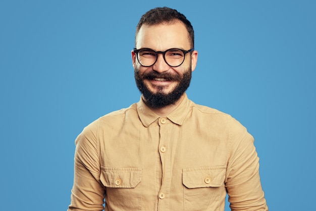 Cheerful adult businessman looking at camera isolated over blue background