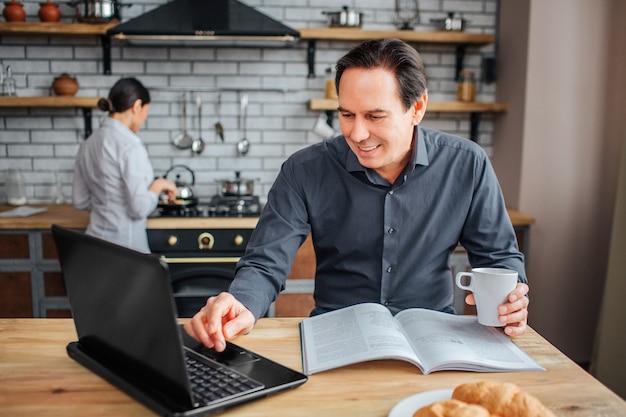 Cheerful adult man sit at table in kitchen.