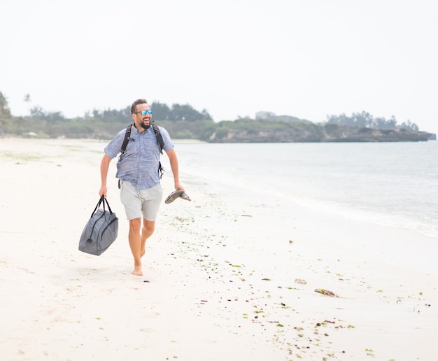 Cheerful adult man with bag having fun on the tropical beach