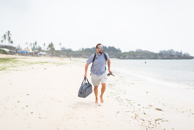 Cheerful adult man with bag having fun on the tropical beach