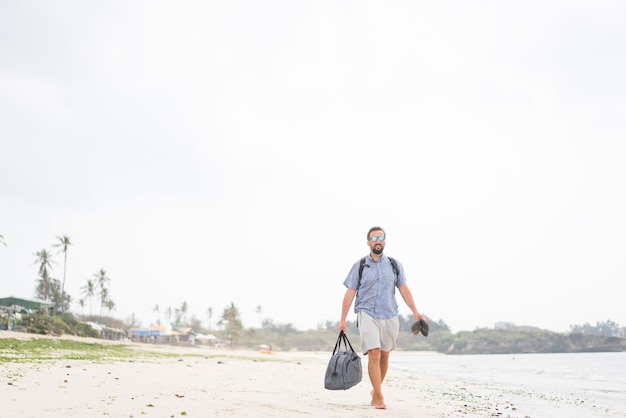 Cheerful adult man with bag having fun on the tropical beach