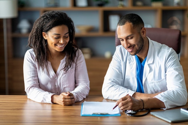 Cheerful african american doctor and patient sitting at\
table