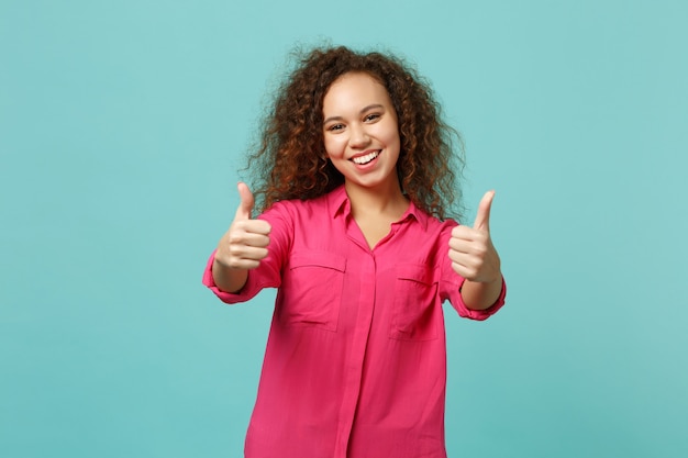 Ragazza afroamericana allegra in abbigliamento casual che mostra i pollici in su, guardando la macchina fotografica isolata sul fondo della parete blu turchese in studio. persone sincere emozioni, concetto di stile di vita. mock up copia spazio.