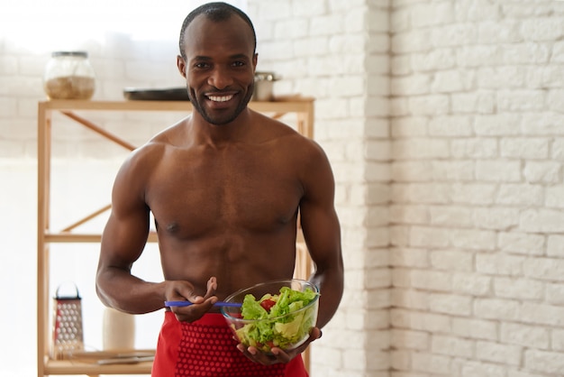 Веселый афроамериканец возбуждает салат на кухне