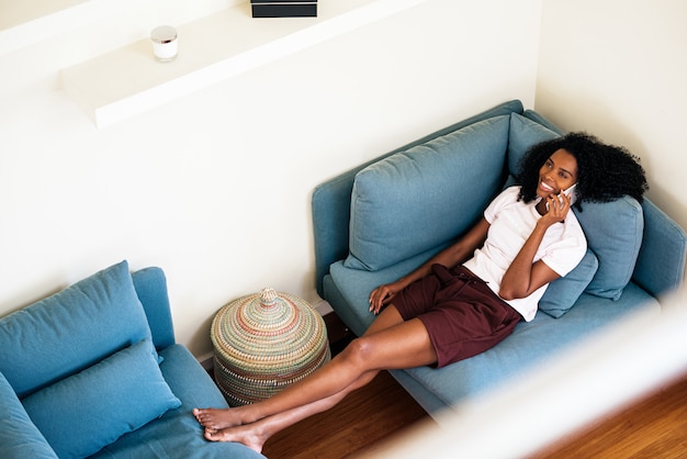 Cheerful African American woman calling on smartphone while resting at home