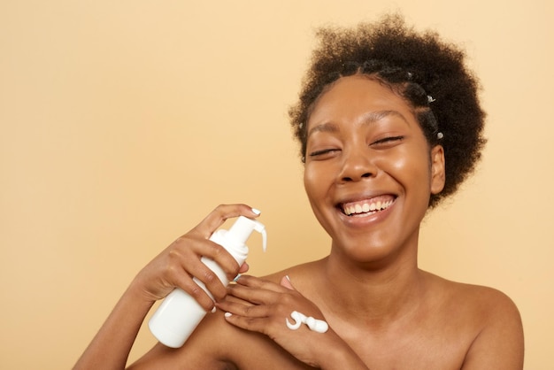 Photo cheerful african american woman with cleansing foam bottle in studio