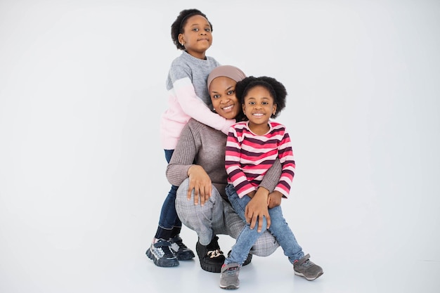 Cheerful african sisters playing with muslim mother in hijab in studio