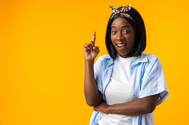 Cheerful african woman points away on copy space against yellow wall