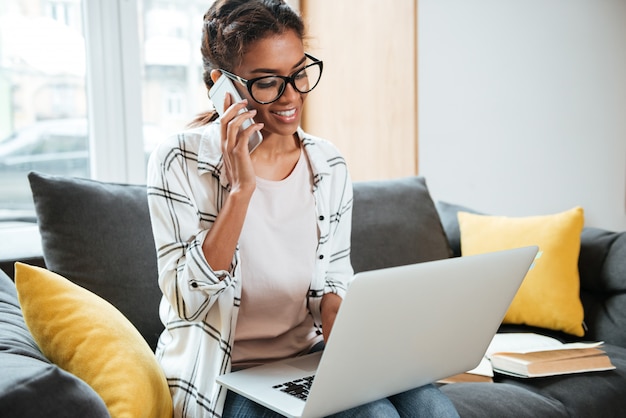 Donna africana allegra che utilizza computer portatile che si siede nella biblioteca