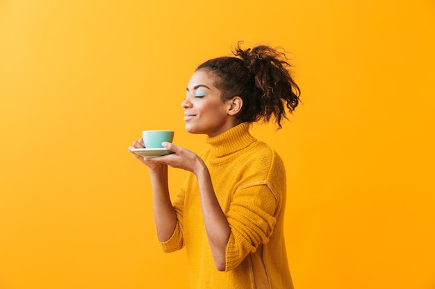 Photo cheerful african woman wearing sweater holding cup on a saucer isolated