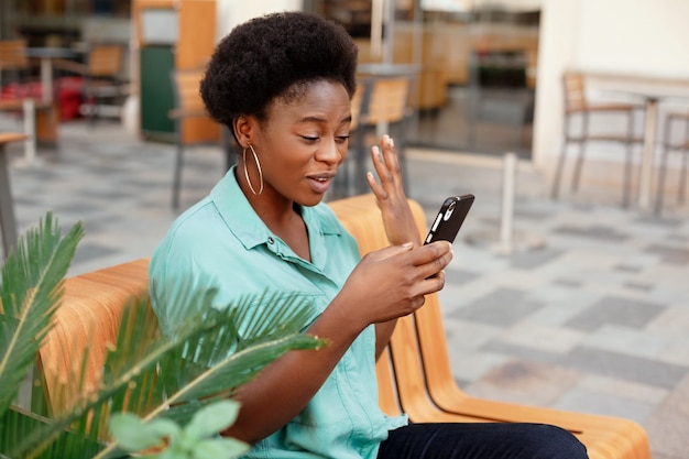 Photo cheerful african woman writes a message on her phone outdoors.