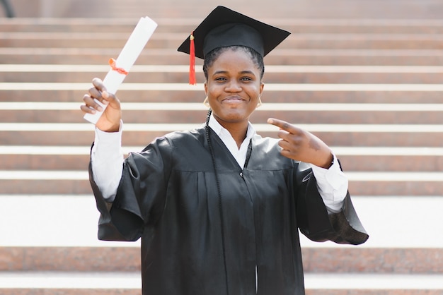 Cheerful afro american female graduate standing in front of university building