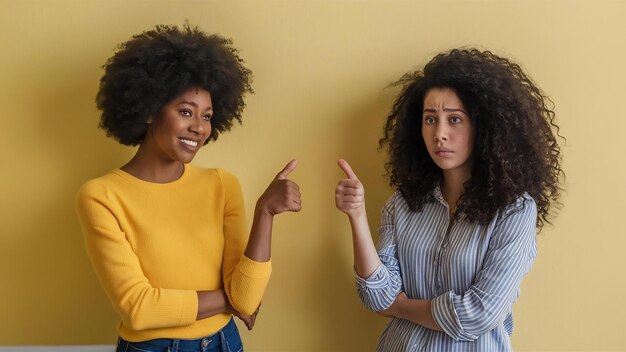 Cheerful afro american woman and her sad curly haired sister point thumbs at each other express dif