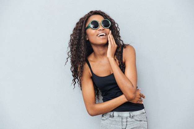 Cheerful afro woman in glasses posing over gray wall