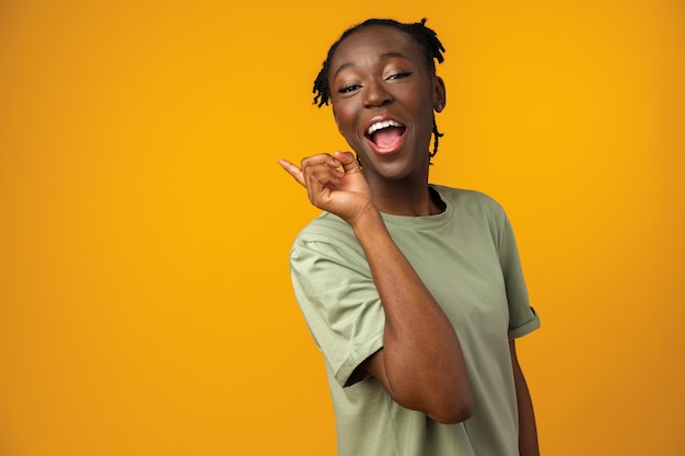 Cheerful Afro woman points to copy space in yellow studio